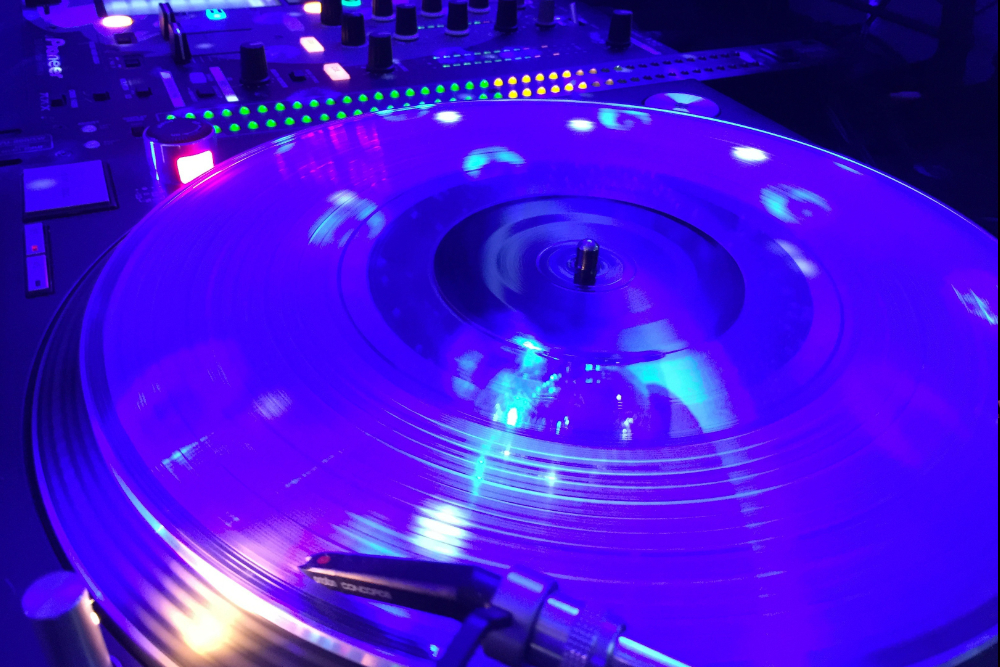 DJ facing a crowd at his deck. Photo with a purple hue