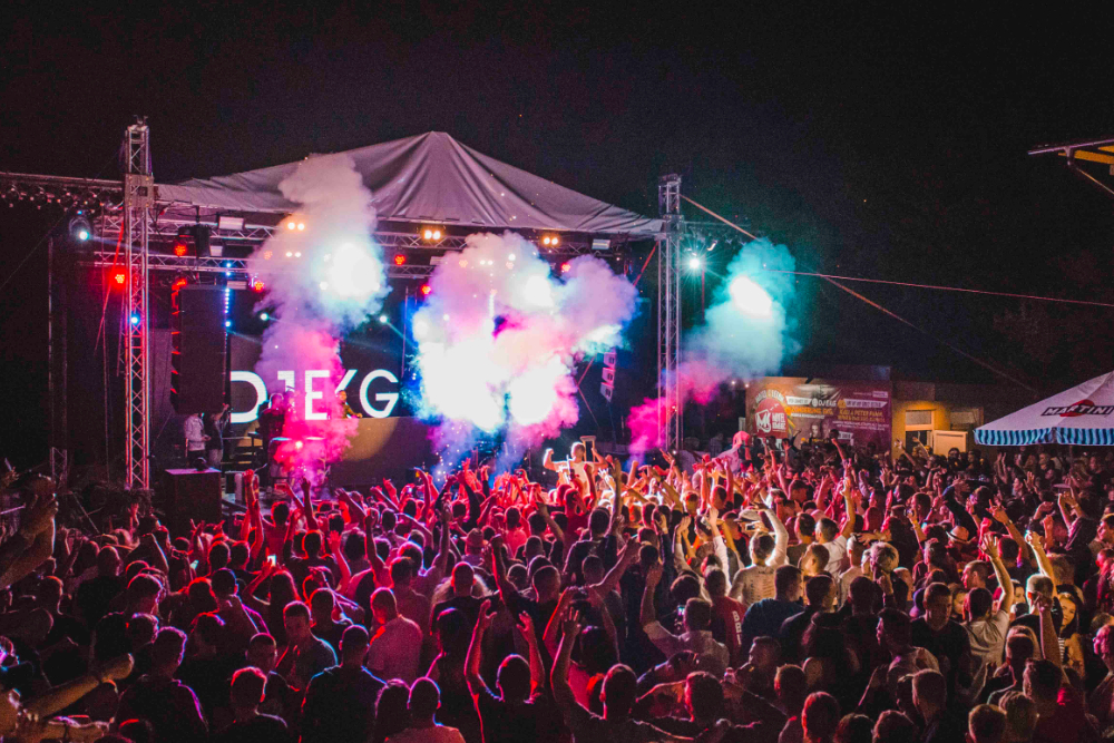 Back of a man at a concert. Hes wearing a beanie hat and a baggy denim jacket with studs. Photo with a purple hue